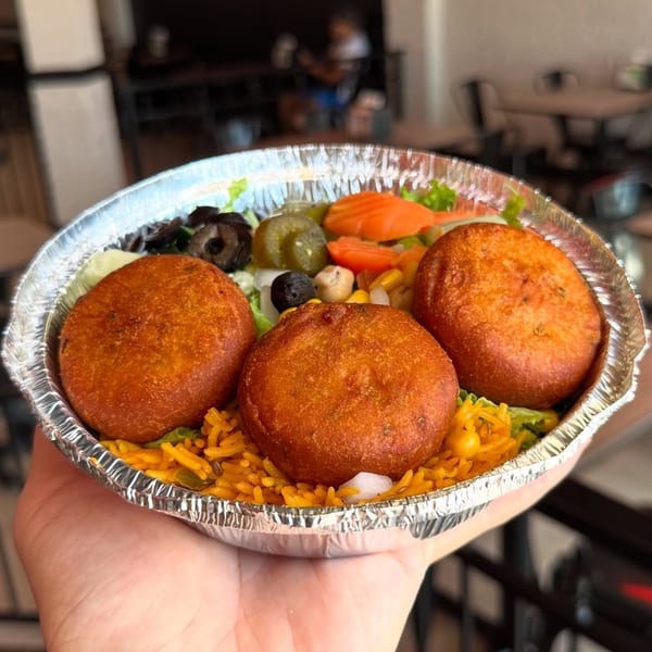 Three golden fried fritters with yellow rice and fresh salad in a foil takeout container.