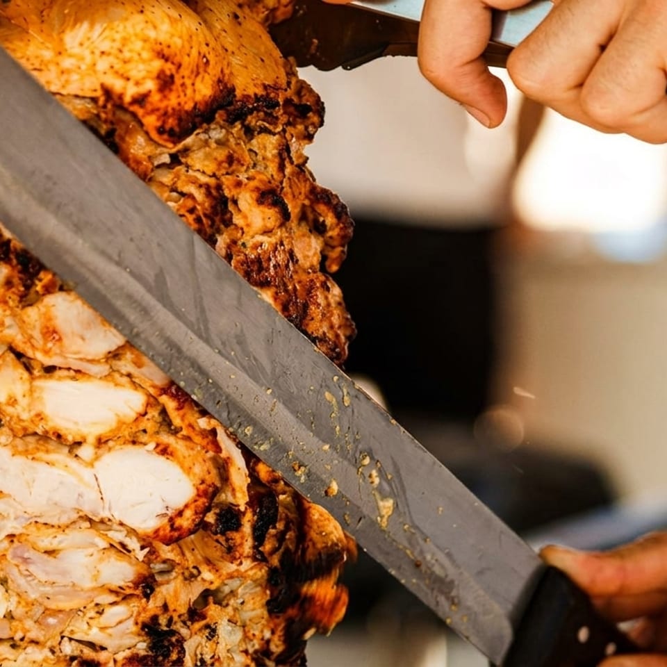 A chef's hands expertly carving juicy, seasoned chicken from a vertical rotisserie skewer.