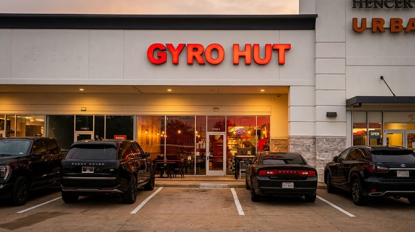 Exterior view of Gyro Hut restaurant with a red illuminated sign and parked cars in front.
