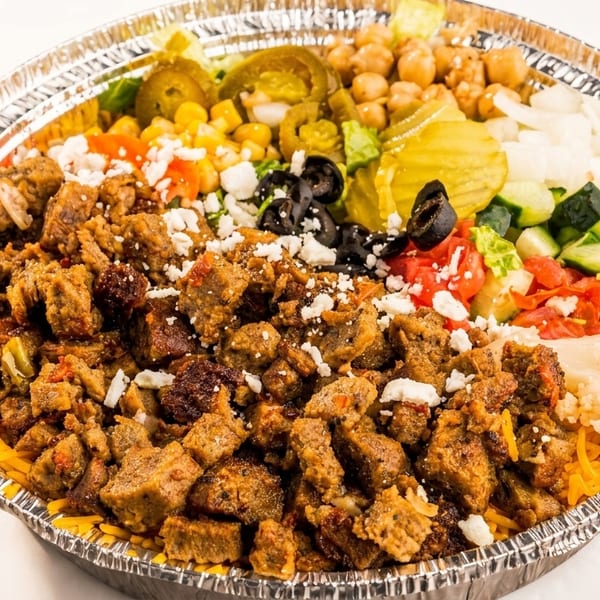 A large foil container filled with gyro meat, rice, chickpeas, salad, and various toppings.