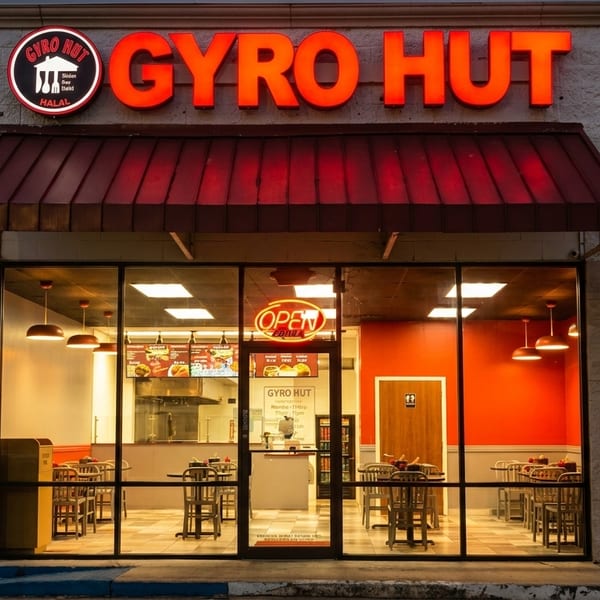 Exterior of Gyro Hut restaurant at dusk, with bright red signage and illuminated interior seating.