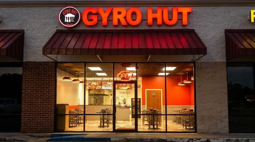 Exterior of Gyro Hut restaurant at dusk, with bright red signage and illuminated interior seating visible.