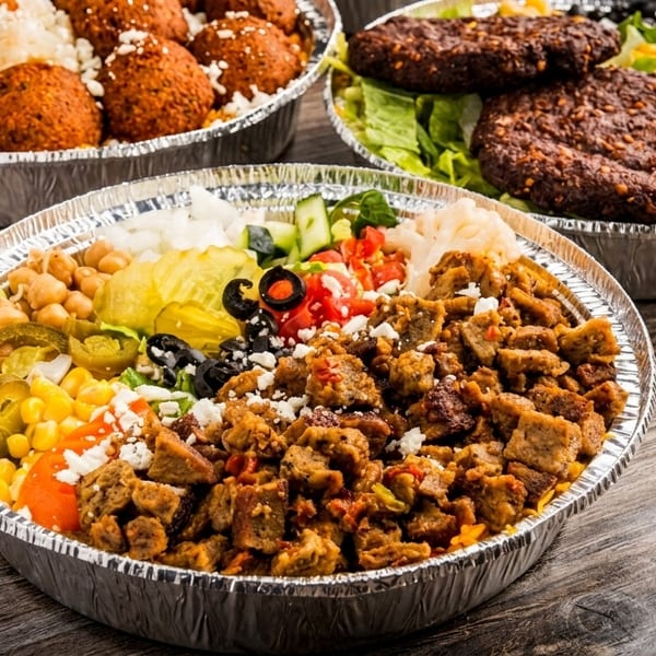 Three foil containers of Mediterranean food, including gyros, falafel, and a salad with patties.