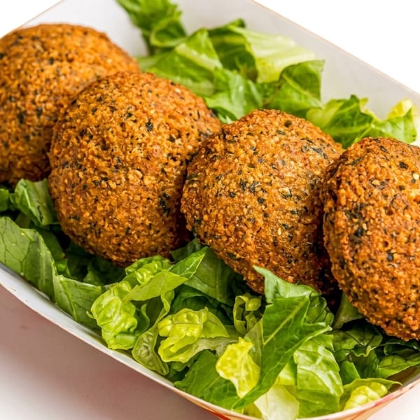 Four golden-brown falafel balls resting on a bed of fresh green lettuce in a white paper tray.
