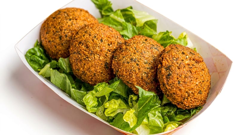 Four golden-brown falafel balls resting on a bed of fresh green lettuce in a white paper tray.