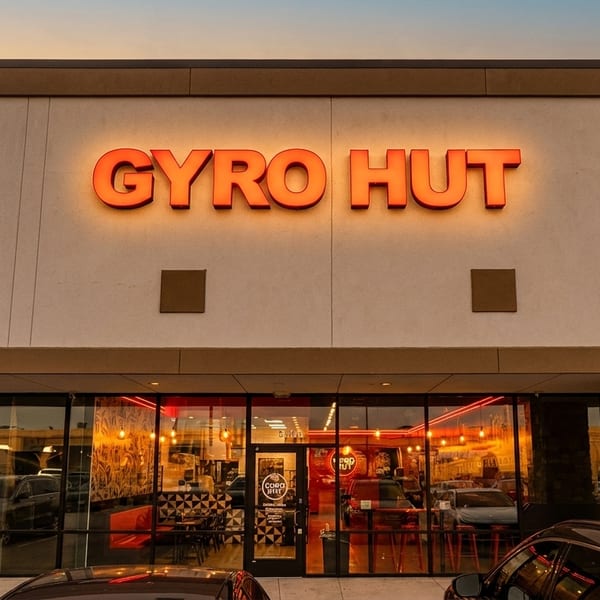 The exterior of Gyro Hut restaurant at dusk, with its bright orange sign illuminated above large windows.