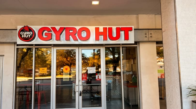 Exterior of Gyro Hut restaurant with a red sign and glass doors reflecting autumn trees.