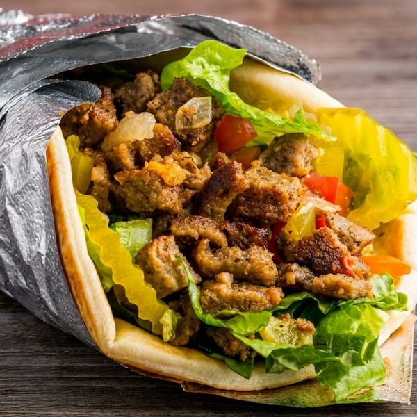 A gyro sandwich, wrapped in foil, filled with meat, lettuce, tomatoes, and pickled peppers.