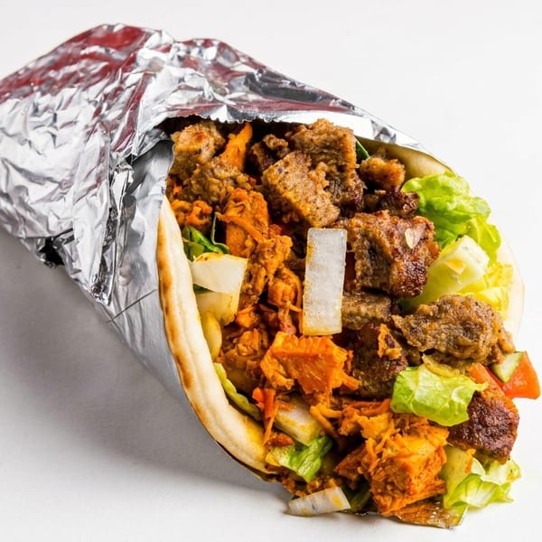 A foil-wrapped gyro, filled with meat, lettuce, onions, and tomatoes, on a white background.